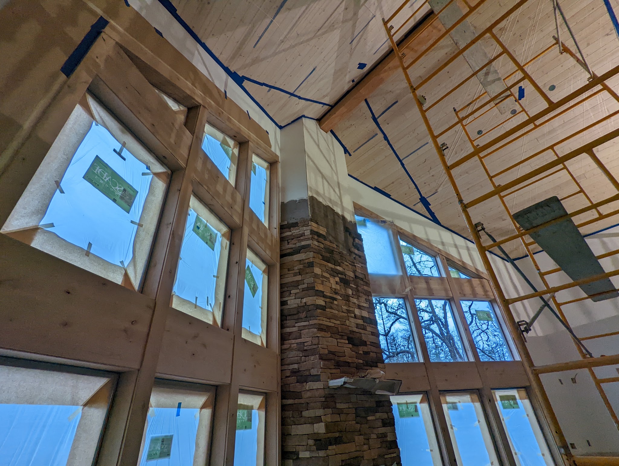 A vaulted great room with a stone fireplace column and floor-to-ceiling windows
