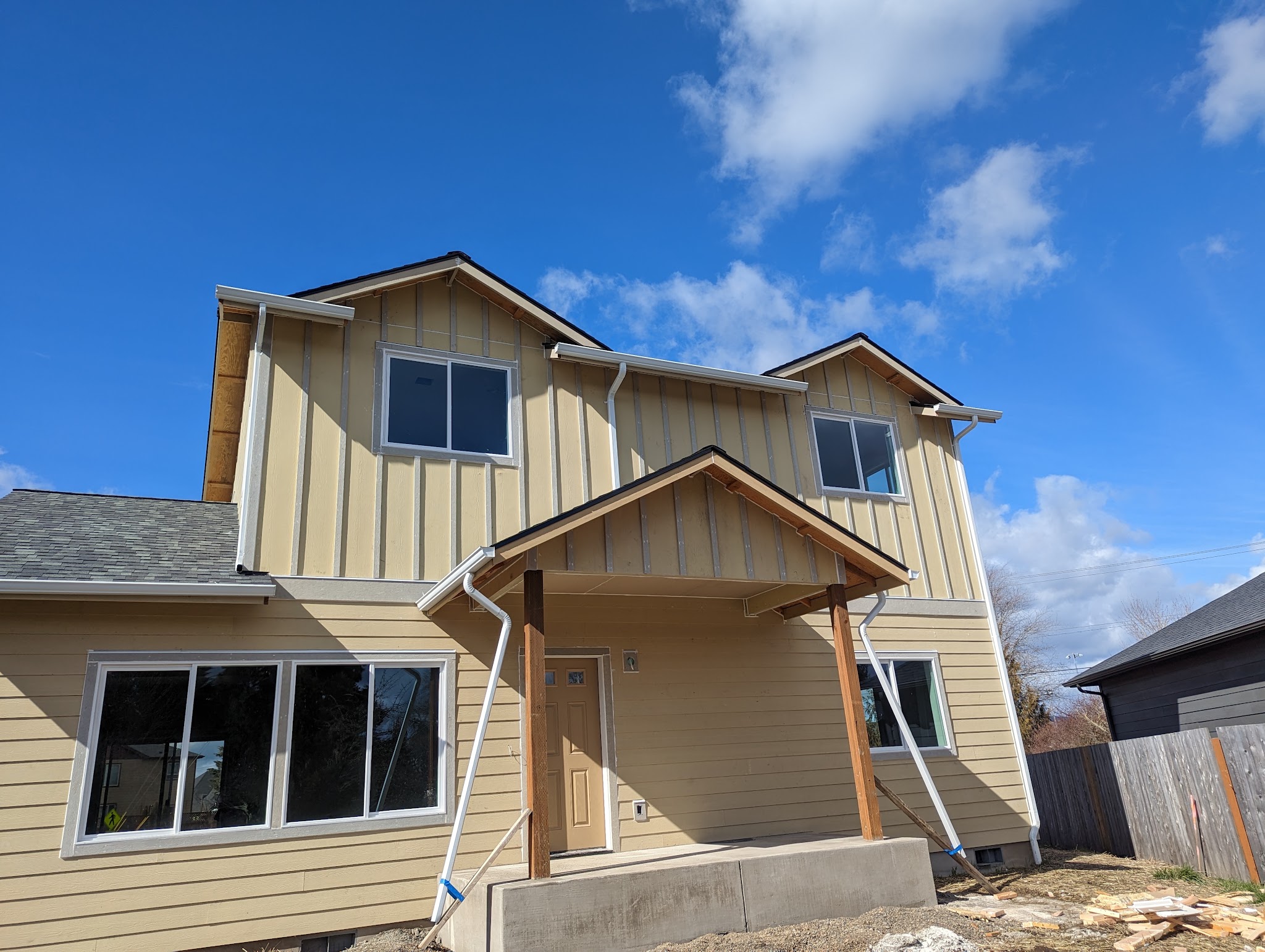A nearly finished two-story new-build home with board-and-batten siding under a blue sky